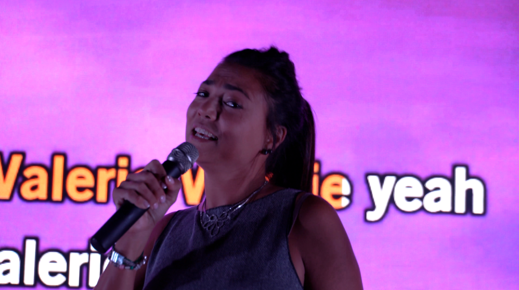 Une candidate chante au micro devant l'écran de paroles