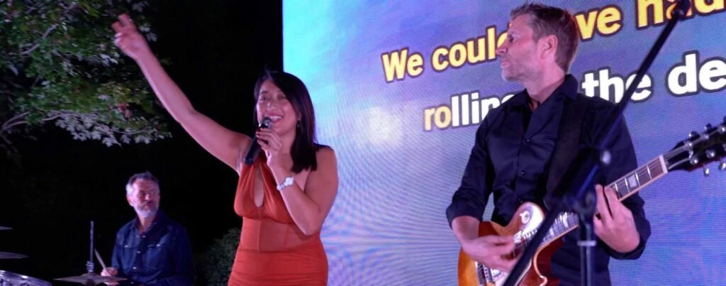 Une candidate en robe rouge chante avec le guitariste à ses côtés