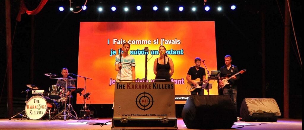 Un homme et une femme chantent au micro sur la grande scène, écran de paroles orange