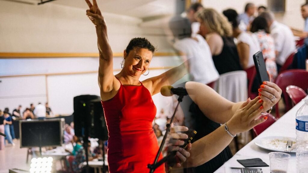 The band's singer with her arm raised and, in the same shot, the audience at a company evening, smartphones in hand