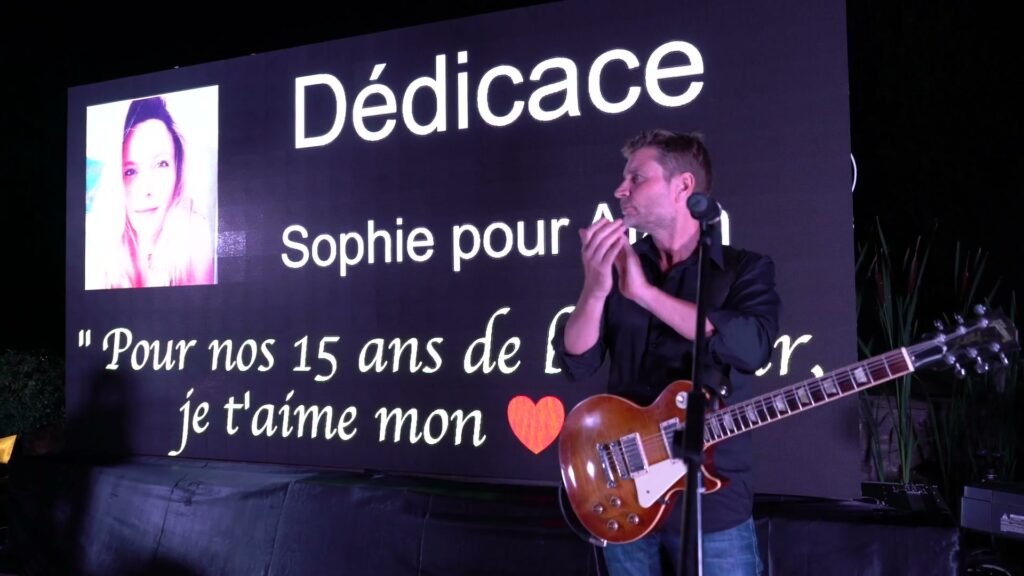 A dedication is shown on the big screen during the evening, and the guitarist applauds