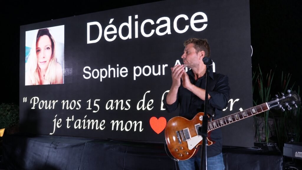 Le guitariste devant une dédicace projetée sur grand écran — image retouchée