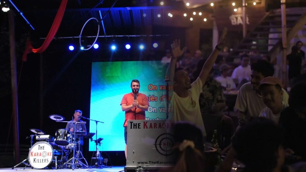 The band on the open-air stage and the audience singing with their arms raised, in a single shot