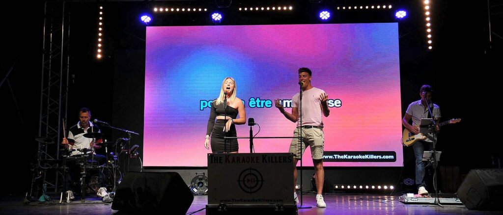 Een duo uit het publiek zingt voor het scherm, de gitarist begeleidt hen