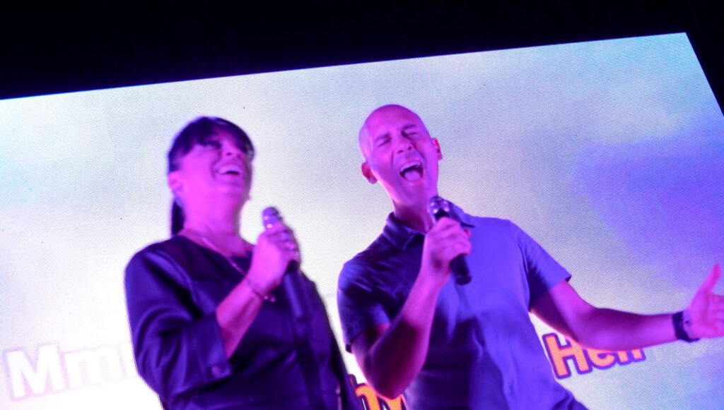 Une candidate et le chanteur du groupe rient en chantant