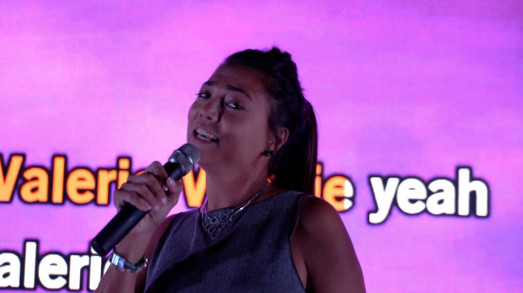 Une candidate chante au micro devant l'écran de paroles
