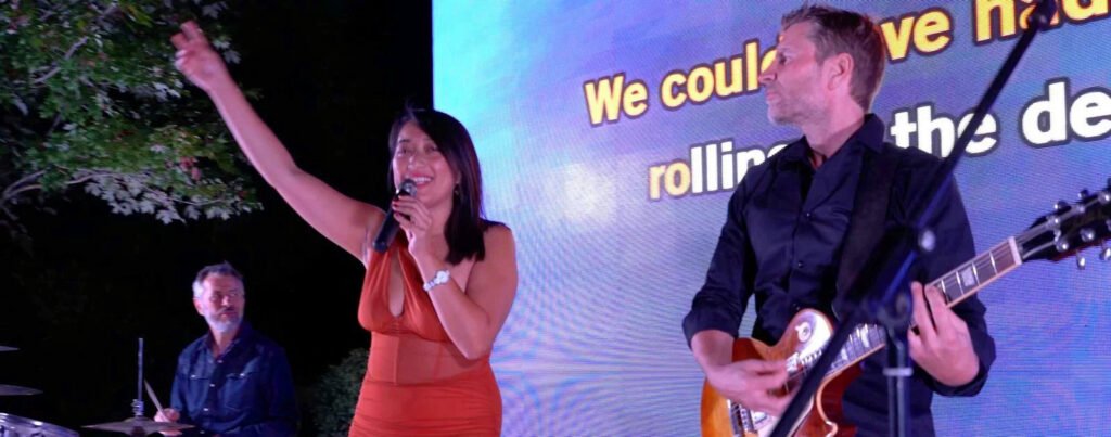 Une candidate en robe rouge chante avec le guitariste à ses côtés